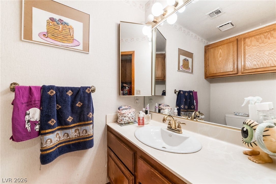 An expansive wall mirror reflects the overhead cabinetry and built-in vanity lighting.