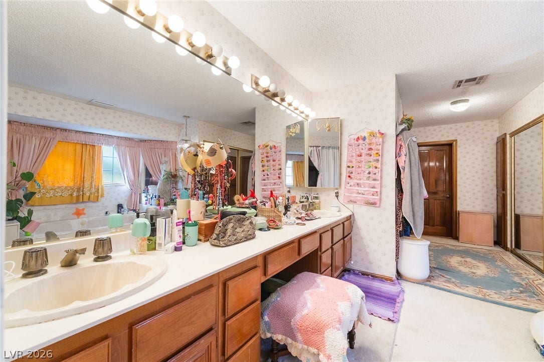 A spacious vanity area with wooden cabinetry and dual basins connects to the primary bath.
