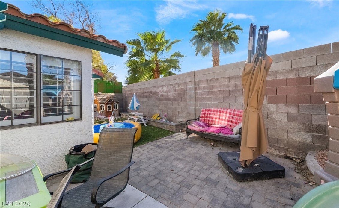 A private paved patio is enclosed by high block walls under towering palm trees.