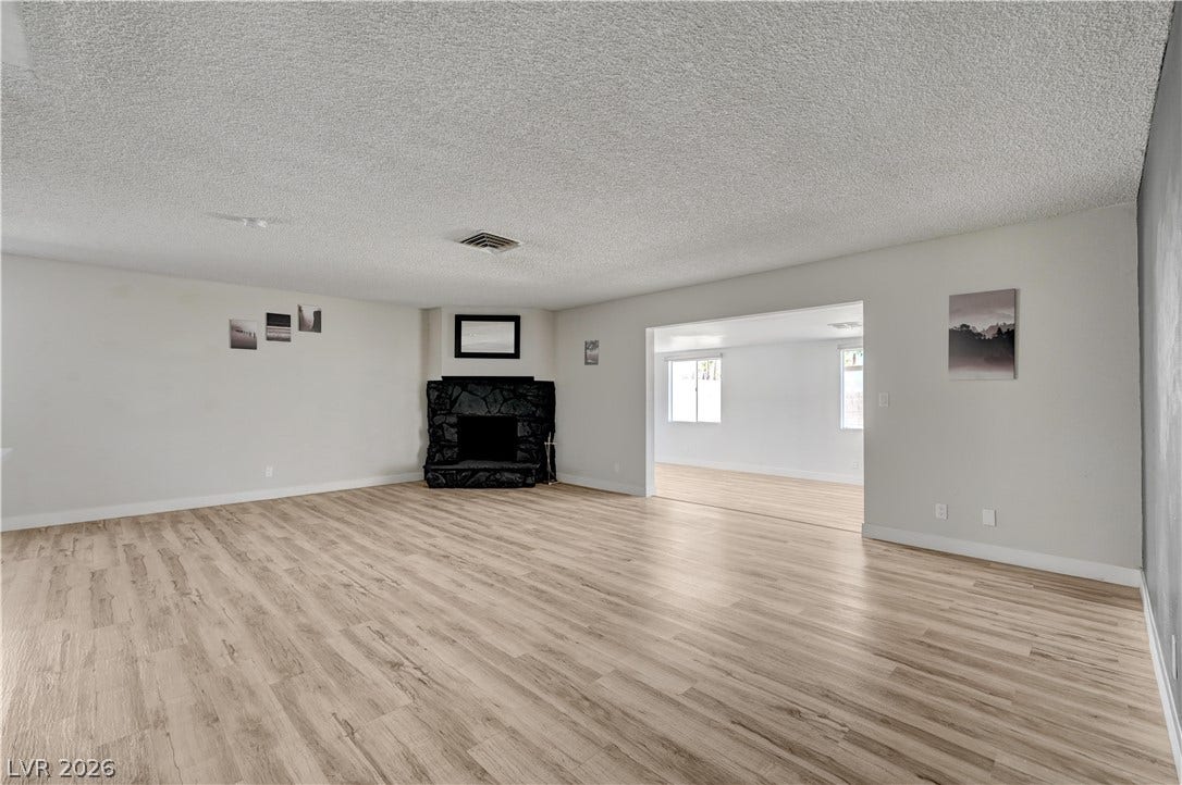4442 Eureka Circle, Las Vegas, NV 89103 An open living room anchored by a dark stone fireplace and wood-look flooring.