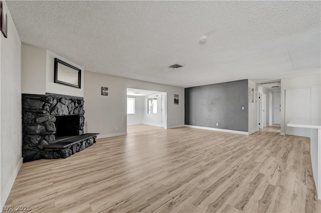 4442 Eureka Circle, Las Vegas, NV 89103 An open living space features wood-patterned flooring and a rustic stone fireplace.