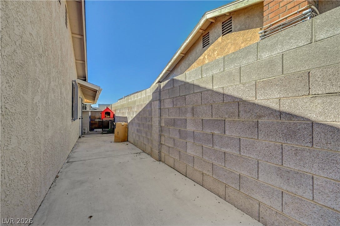 4442 Eureka Circle, Las Vegas, NV 89103 A long concrete side yard features tall stucco and block walls under clear blue skies.