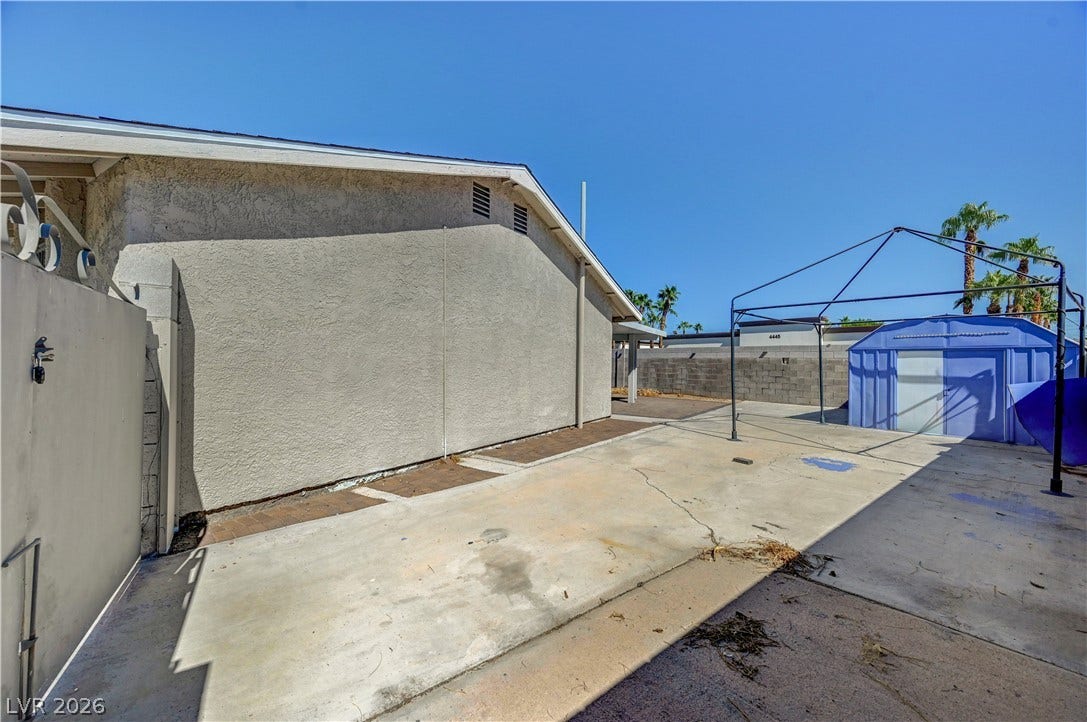 4442 Eureka Circle, Las Vegas, NV 89103 A spacious paved concrete side yard features structured stucco walls and storage solutions under clear blue skies.