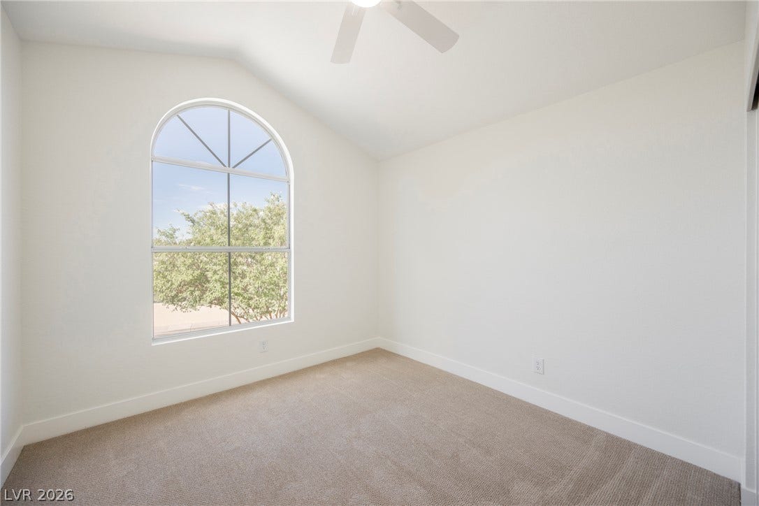 An arched window frames serene leafy views in a carpeted room with vaulted ceilings.