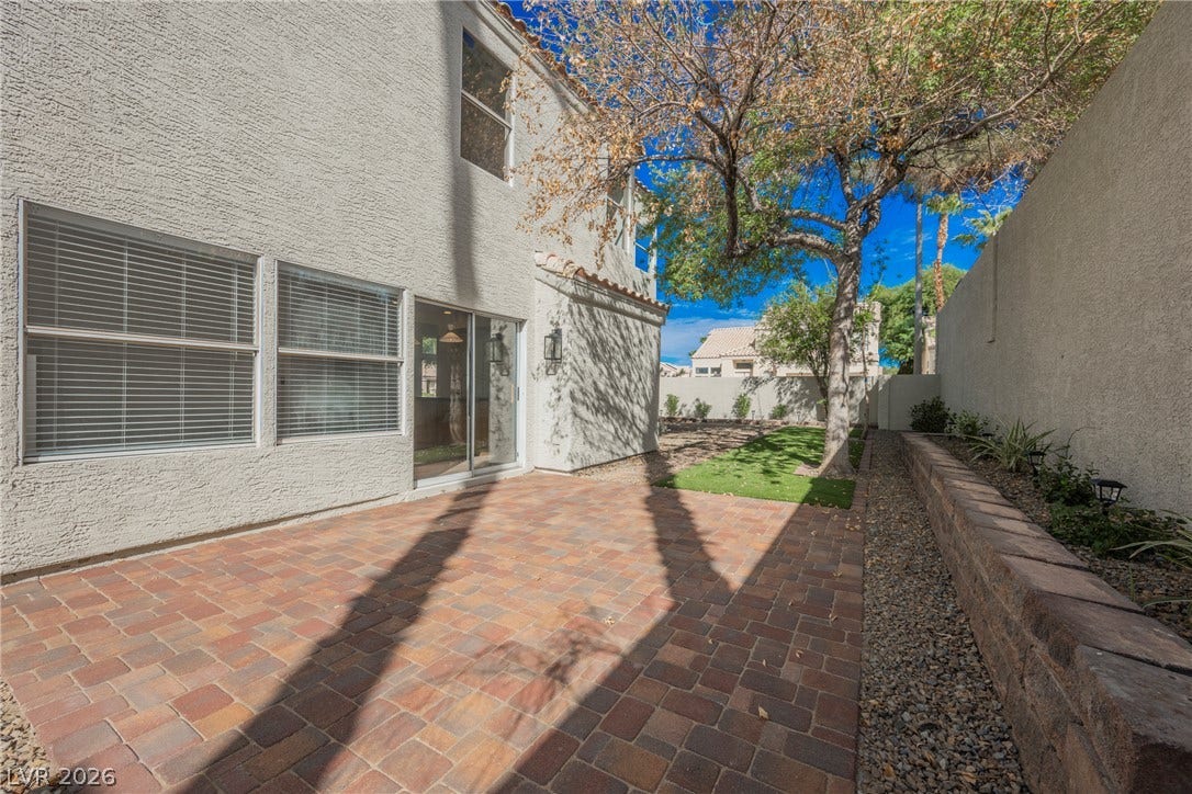 An inviting paver patio extends into a low-maintenance backyard lined with a stone retaining wall.