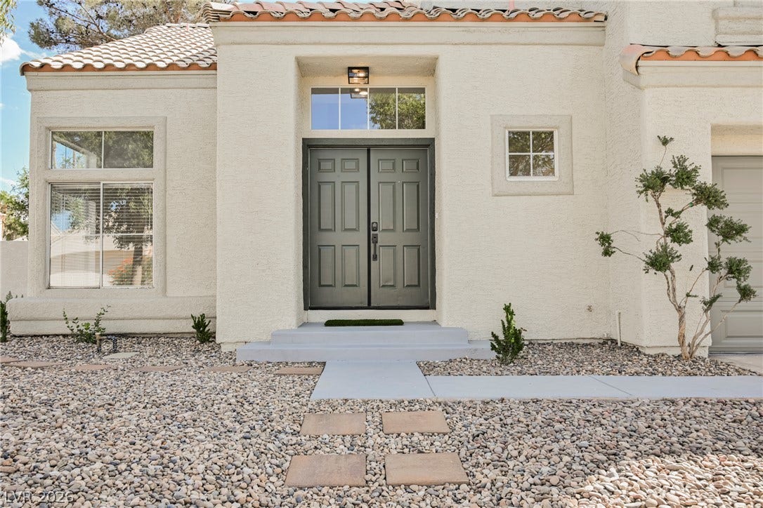 Double entry doors welcome visitors to this classic stucco residence under a tiled roof line.