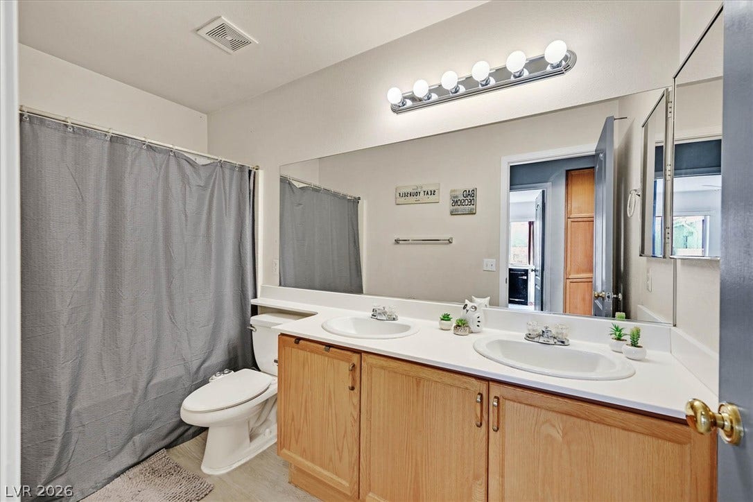 8830 Haviland Road, Las Vegas, NV 89123 An expansive mirror crowns a double vanity with wooden cabinetry in this functional bathroom.
