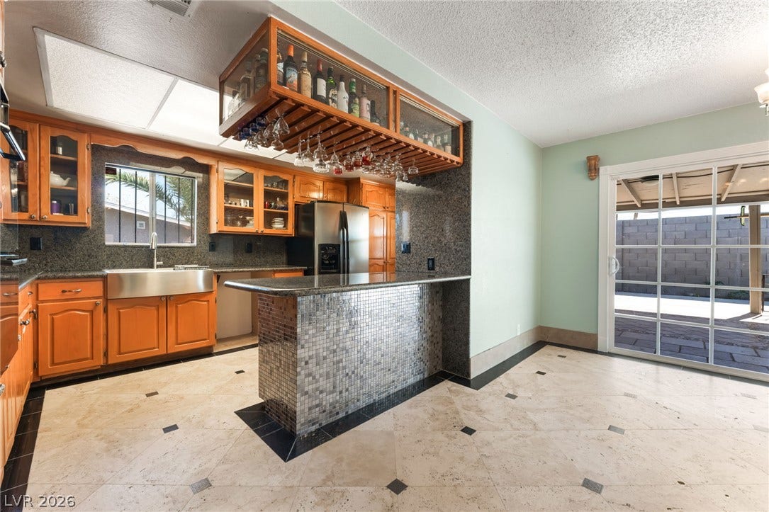 Gleaming stone tile floors underfoot lead directly to a custom breakfast bar and patio door.