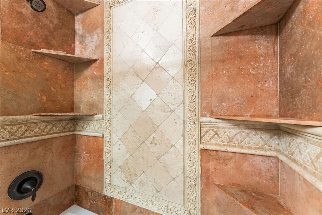 Ornate stone tilework and built-in corner shelving line this custom shower enclosure.