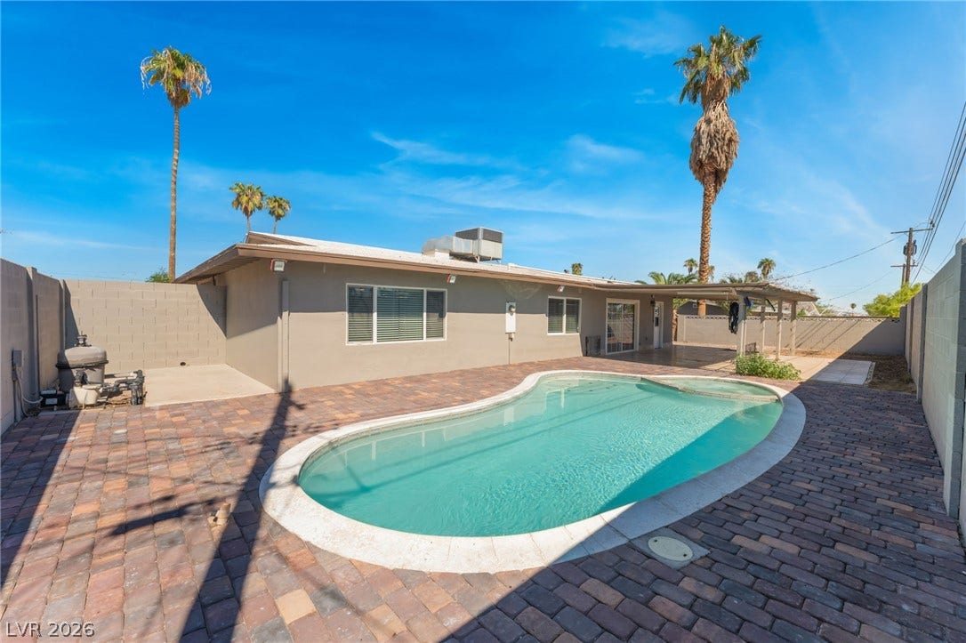 An inviting backyard oasis features a curved swimming pool surrounded by extensive paver decking.
