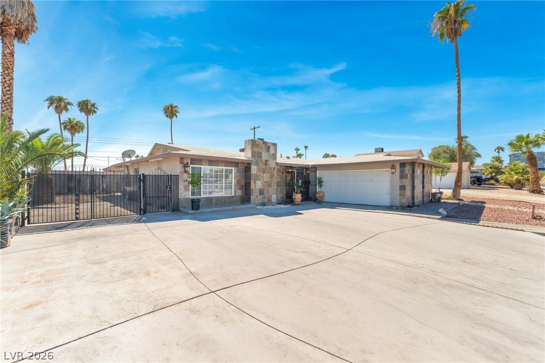 A spacious concrete driveway leads toward the stone-accented facade under a clear blue sky.