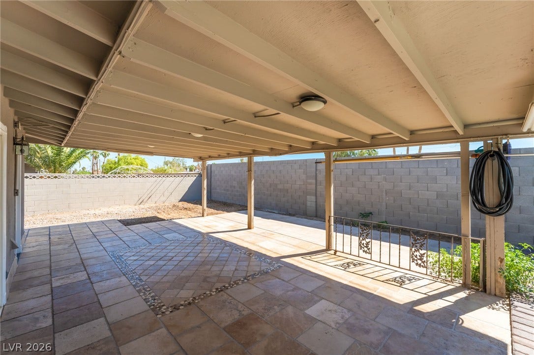 A spacious covered patio features tiled flooring alongside a walled backyard.