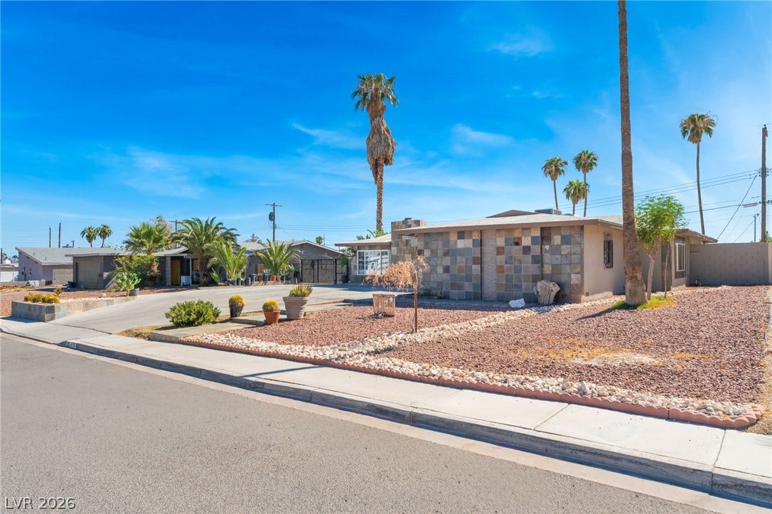 A textured stone facade accents this single-story midcentury home framed by desert landscaping.