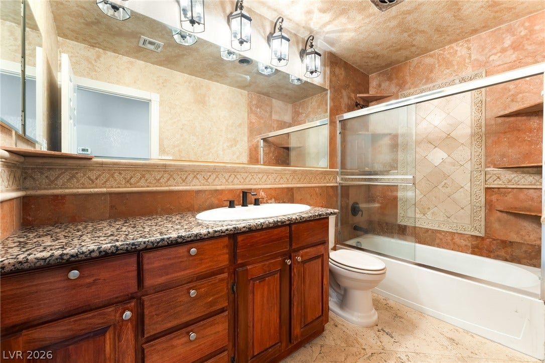 Earthy stone tile walls and rich wood cabinetry define this inviting full bathroom.