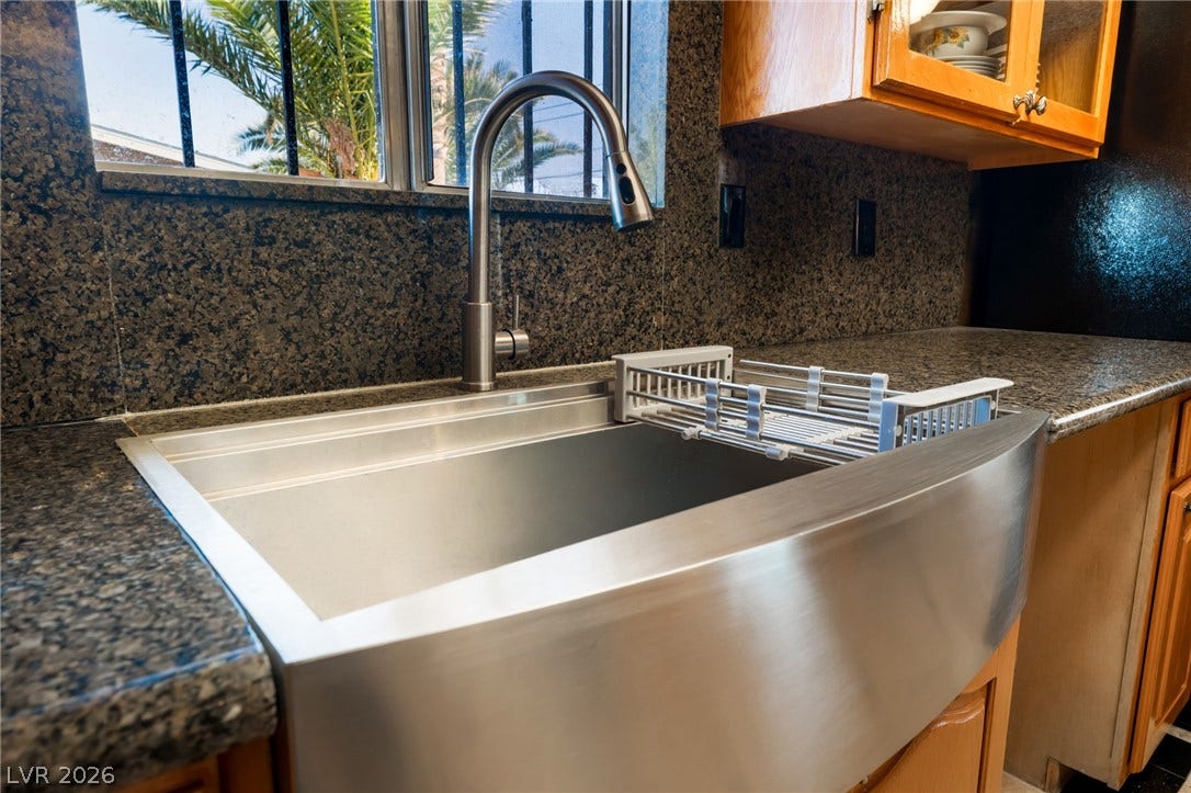 A modern farmhouse sink pairs with sleek stone countertops below a sunny window view.
