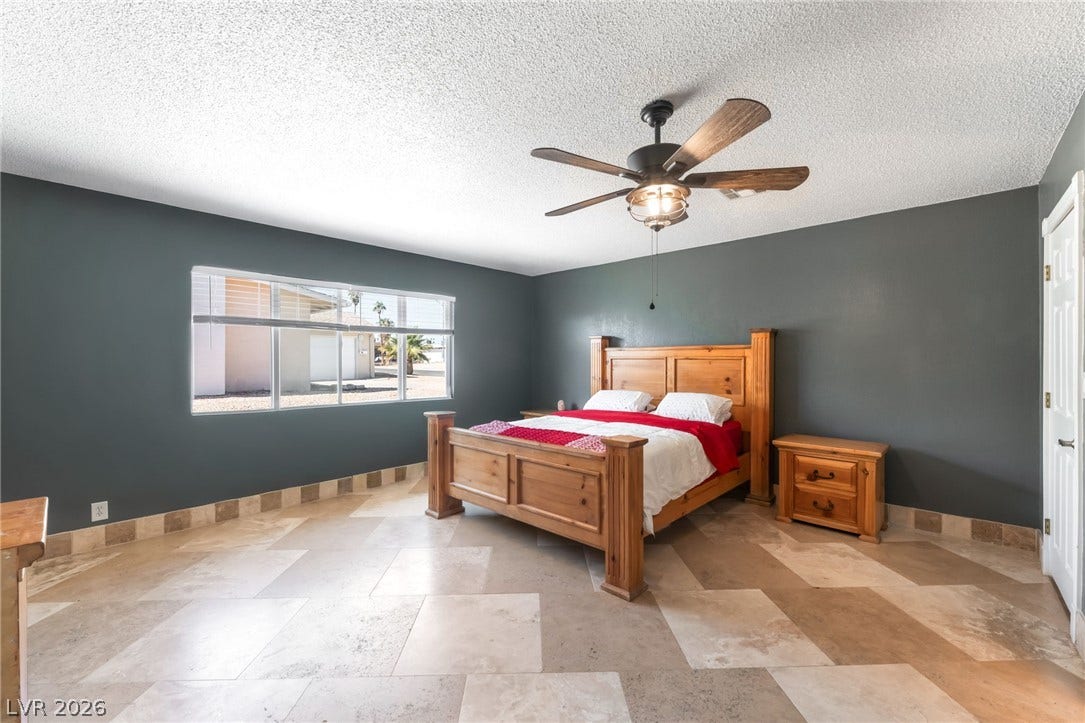 A spacious bedroom features neutral tiled flooring and a wide window letting in natural light.