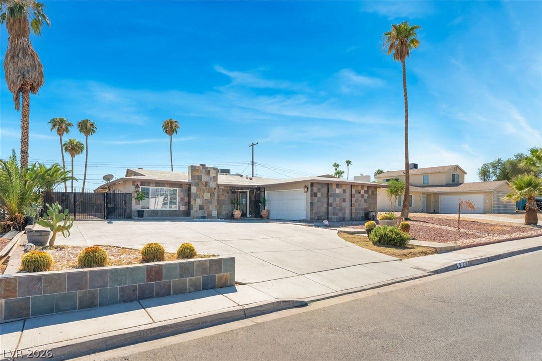 An expansive concrete driveway leads to this mid-century modern facade featuring prominent stone accents.