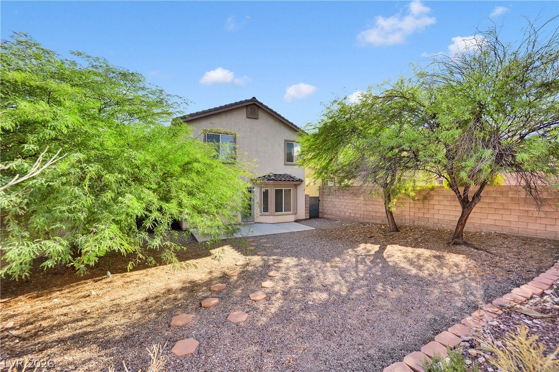 Mature trees frame a private backyard complete with a stone wall and paved patio.