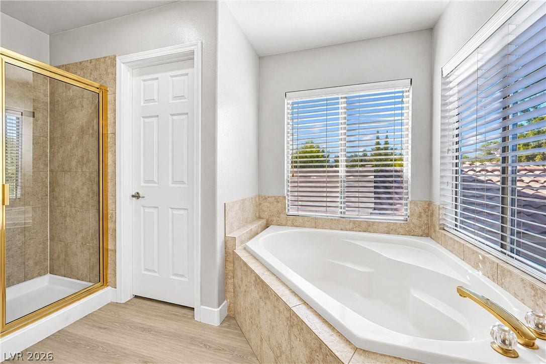 Natural light fills this bathroom featuring a large corner tub and separate tiled shower.