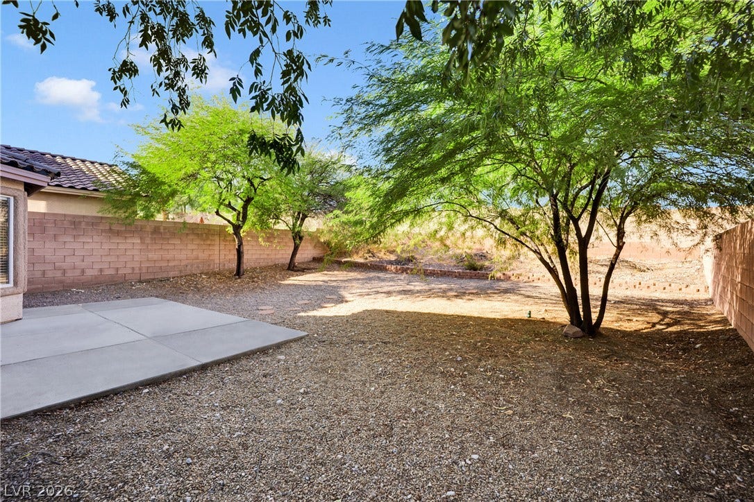 Mature trees shade a low-maintenance backyard enclosed by block fencing.
