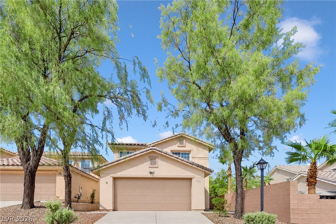 Mature trees frame a welcoming facade leading to the attached garage.