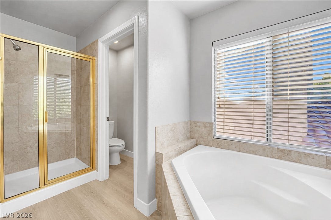 An inviting soaking tub rests beneath a large window in this bright primary bathroom.