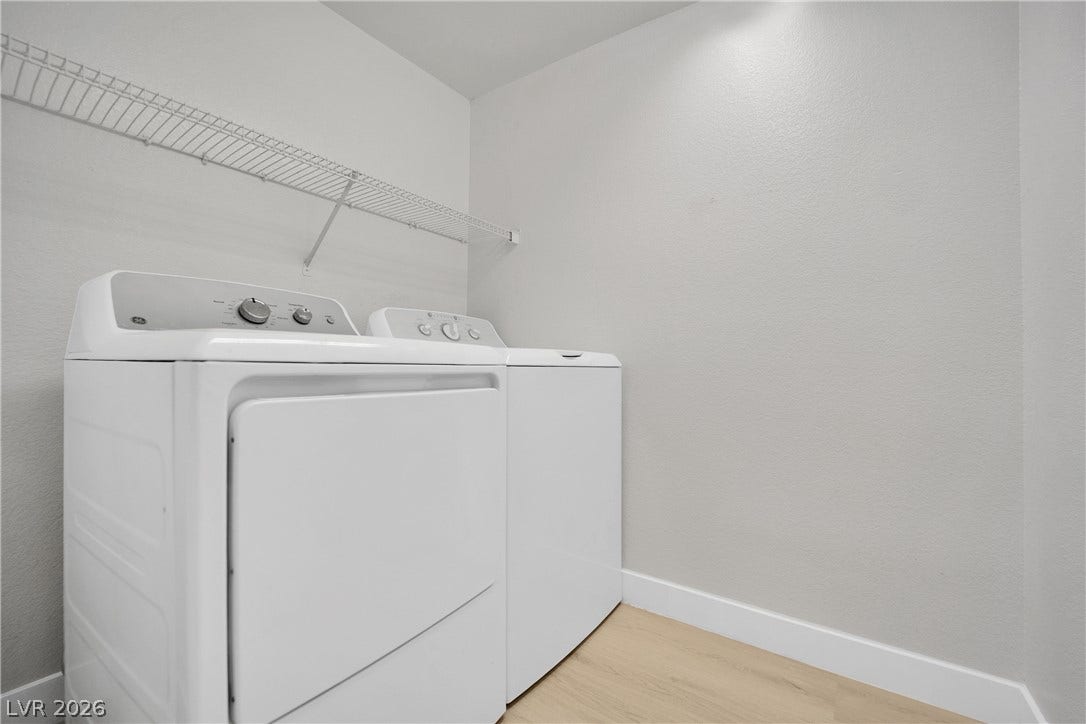 A dedicated laundry space features clean walls, light wood-toned flooring, and overhead wire shelving.