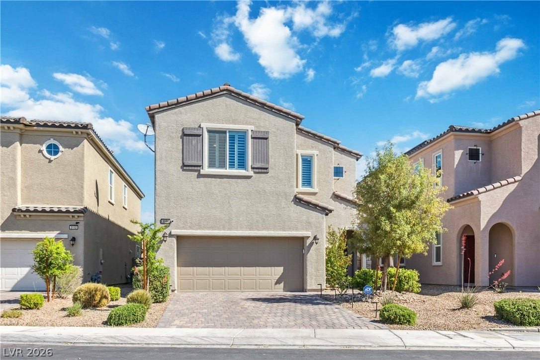 A paved driveway leads to the integrated garage of this stucco multi-level residence.