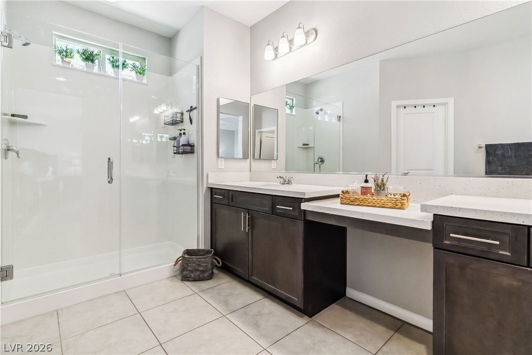 A spacious walk-in glass shower stands beside a sleek dual vanity setup with tiled flooring.
