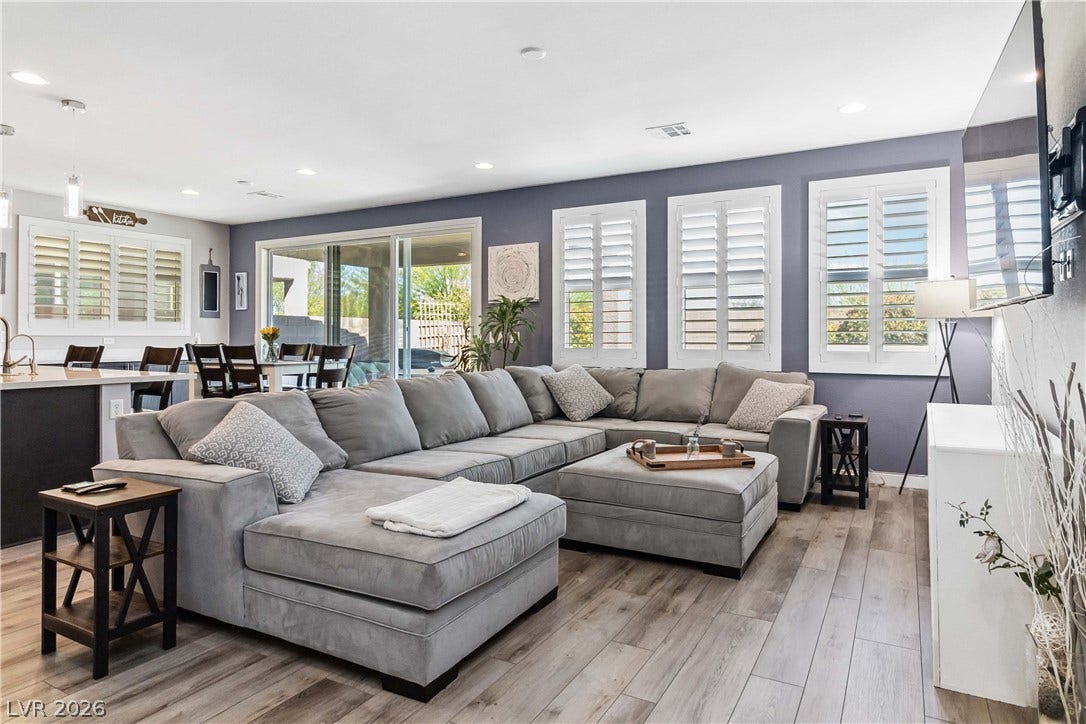 Recessed lighting illuminates this open living space featuring wood-look flooring and plantation shutters.