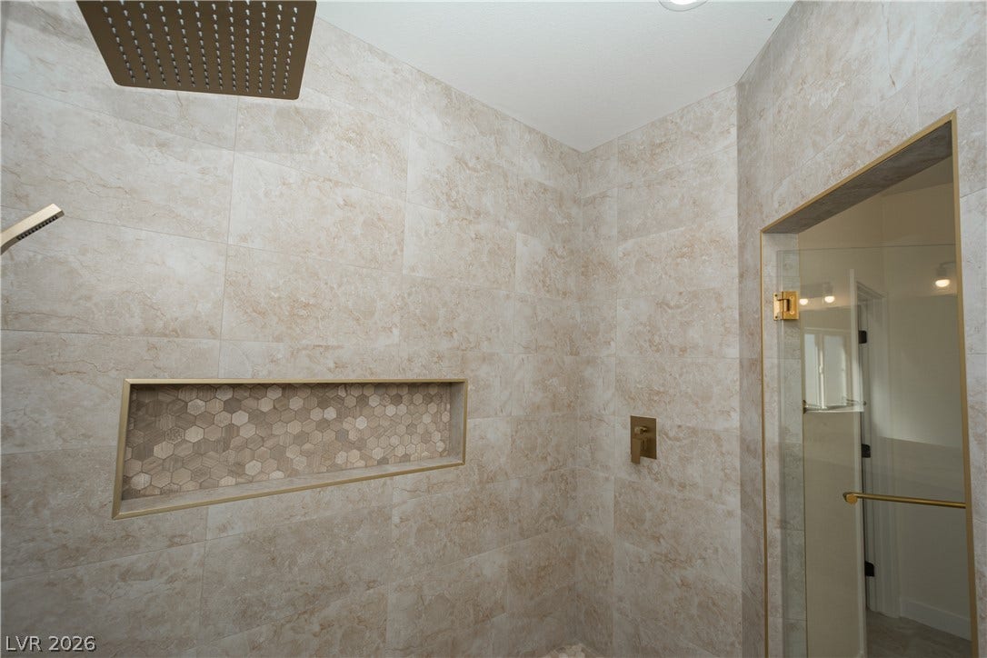 Elegantly tiled walk-in shower features built-in niche shelving and premium gold-toned fixtures.