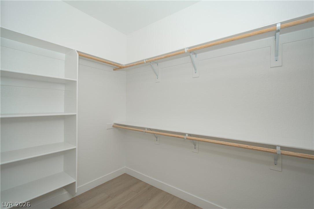 A spacious walk-in closet includes custom built-in shelving, hanging rods, and wood flooring.