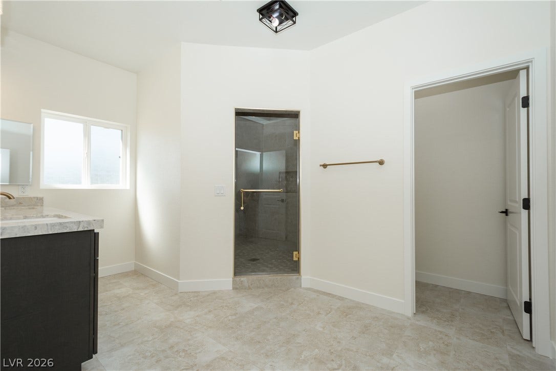 A glass-enclosed walk-in shower highlights this airy bath area with tile flooring.