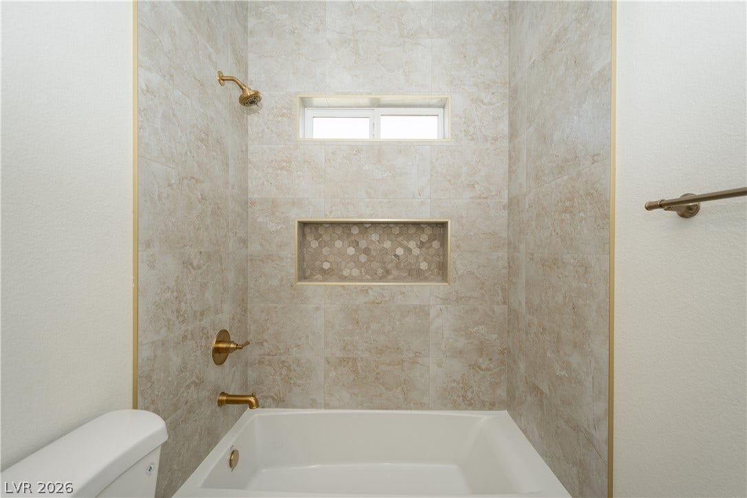 Elegant tile surrounds a modern soaking tub accented by refined gold-toned fixtures.