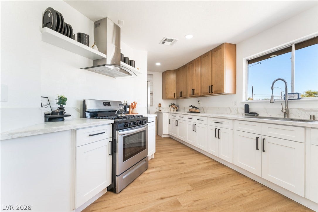 Warm wood flooring complements dual-tone cabinetry and sleek solid-surface countertops in this spacious culinary workspace.