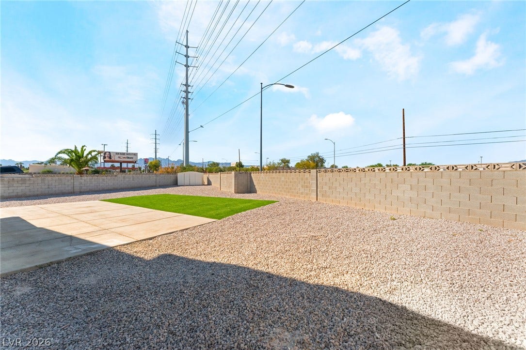 A spacious backyard is enclosed by a secure block wall under a clear sky.