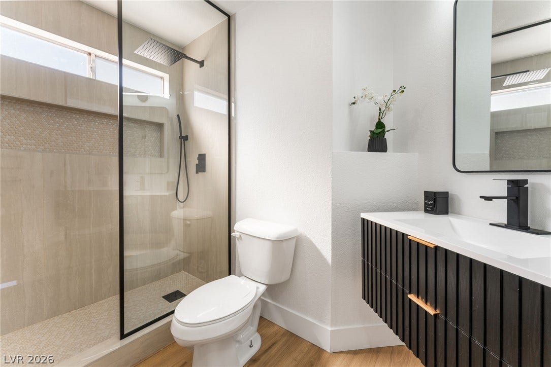 A glass-enclosed walk-in shower complements the floating vanity and warm wood flooring.