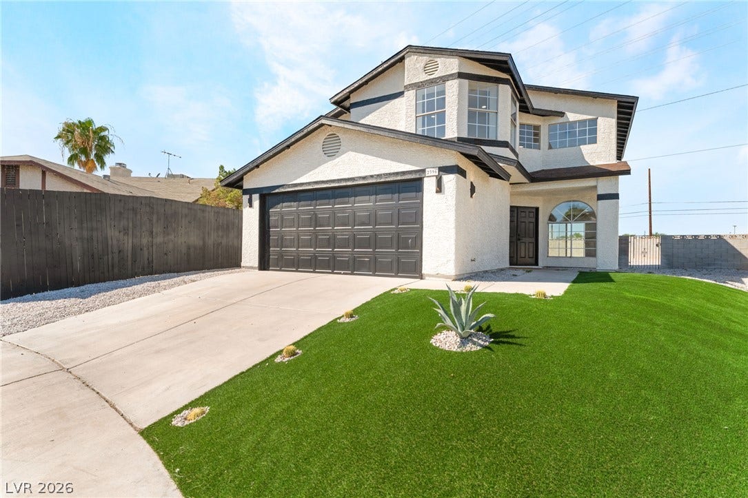An inviting two-story stucco exterior features a concrete driveway and tidy low-maintenance landscaping.