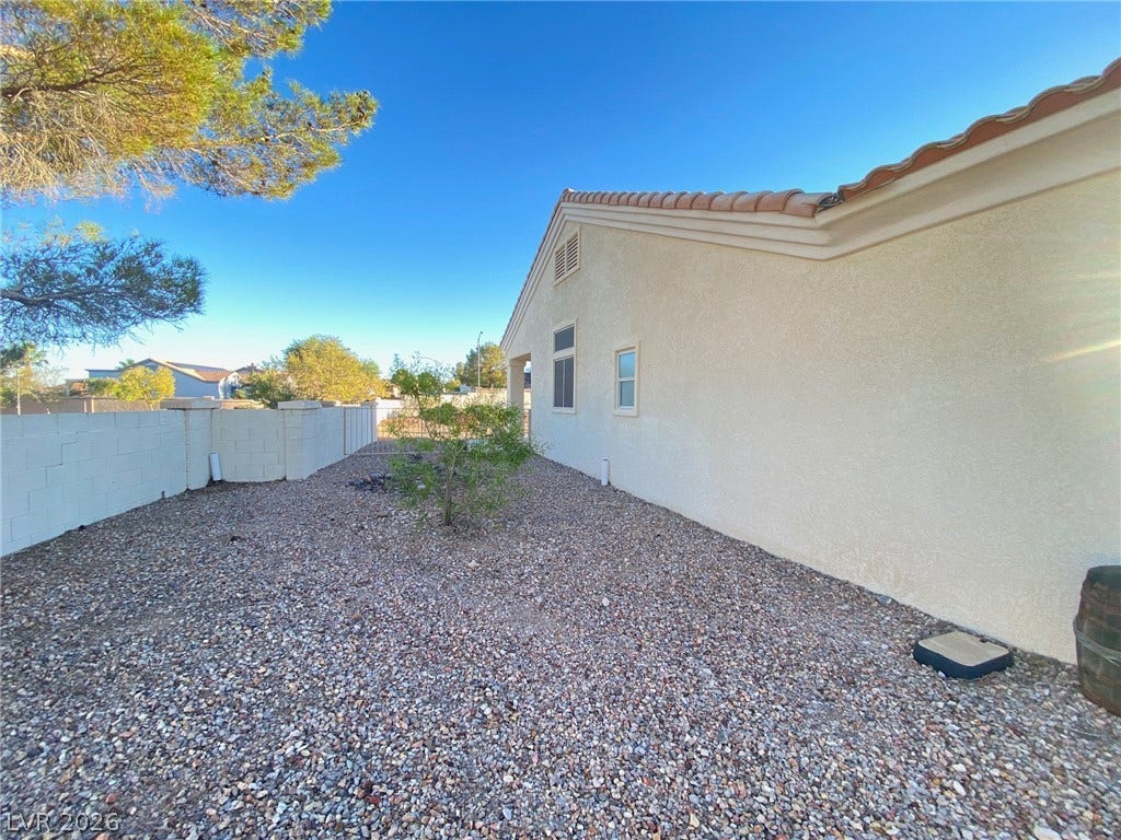 Low-maintenance gravel landscaping spans the side yard alongside the stucco exterior and block fencing.