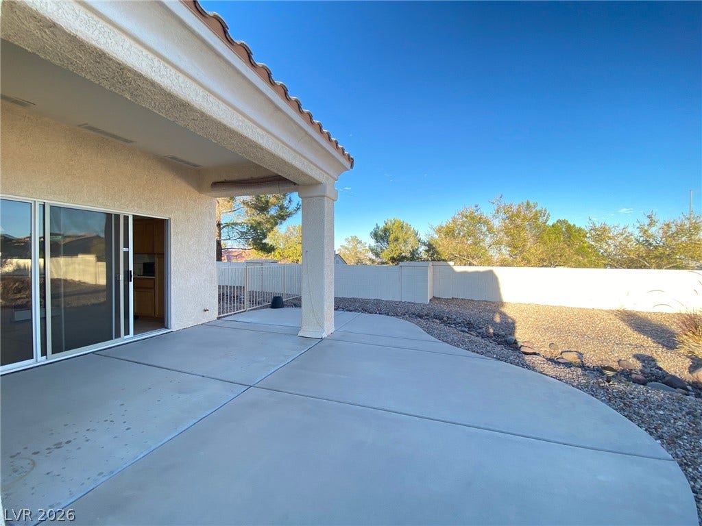 A spacious concrete patio rests beneath a deep covered overhang, overlooking a walled backyard.