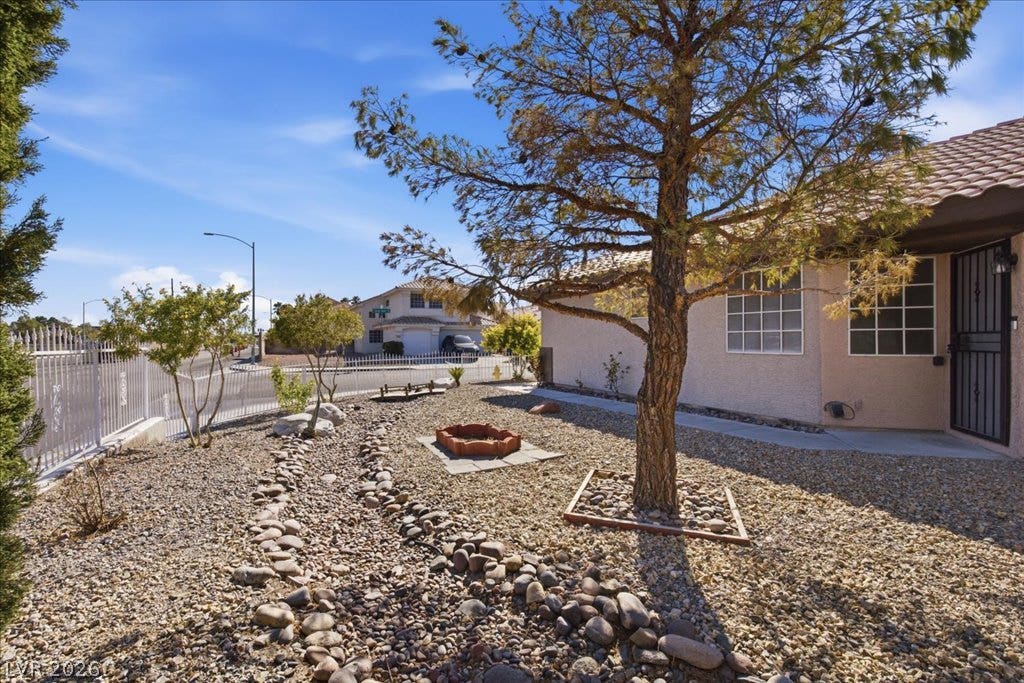 Low-maintenance desert landscaping and mature trees frame the entrance of this stucco home.