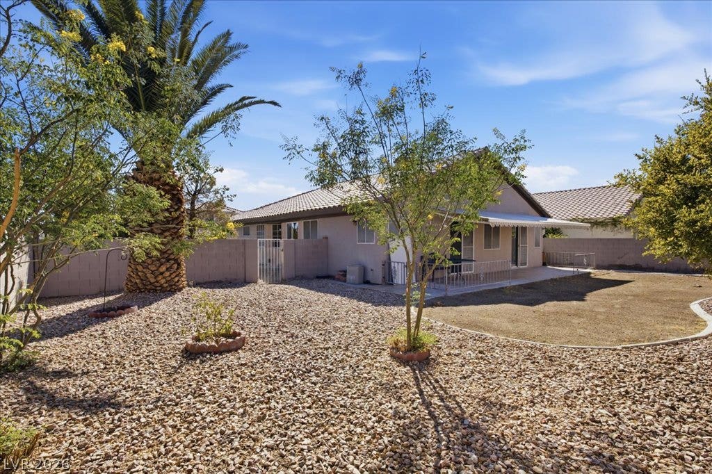 Mature desert landscaping frames a low-maintenance gravel yard with a concrete patio.