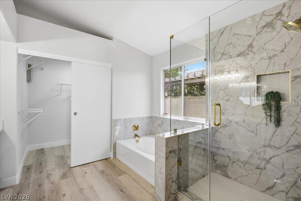 Elegant marble-patterned tile surrounds a glass-enclosed shower and adjacent soaking tub.
