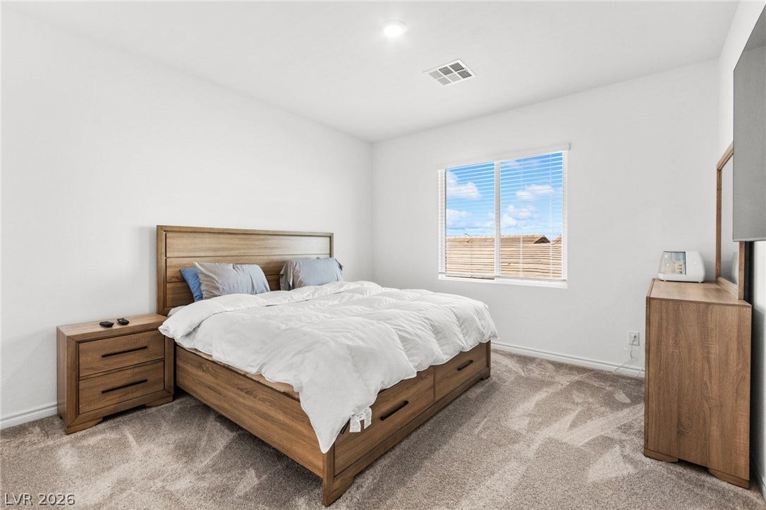 A restful primary bedroom retreat with soft carpeting and natural light filtering through window blinds.