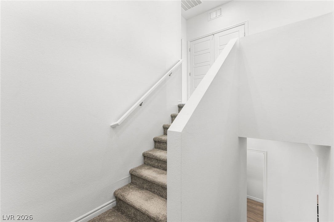 Carpeted stairs ascend to a landing with crisp white walls and a light-filled ambiance.
