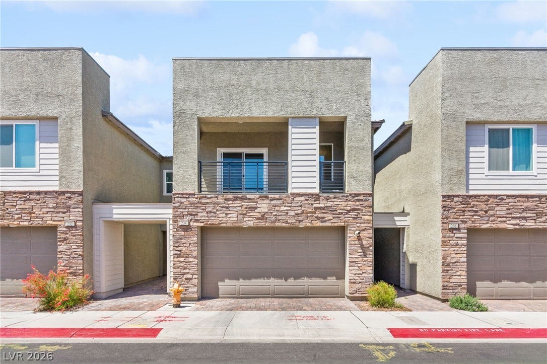 A contemporary townhouse facade presents textured stucco and stacked stone accents, with a central balcony overlooking the street.