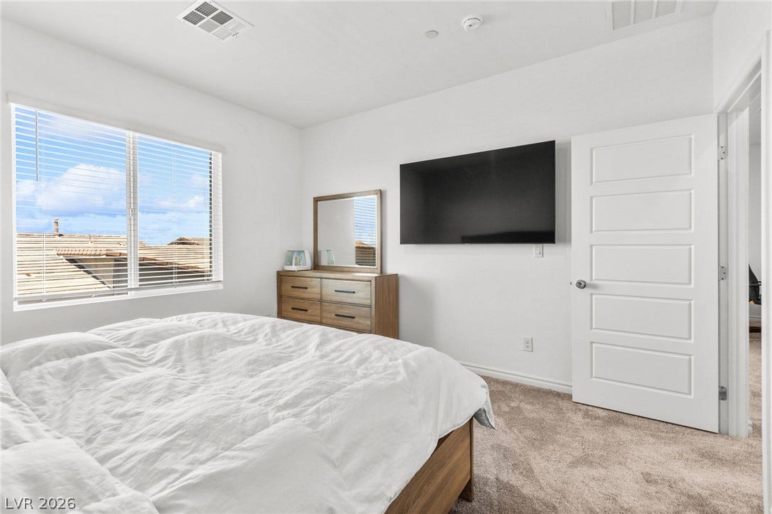 Natural light cascades into this bedroom with plush carpeting.