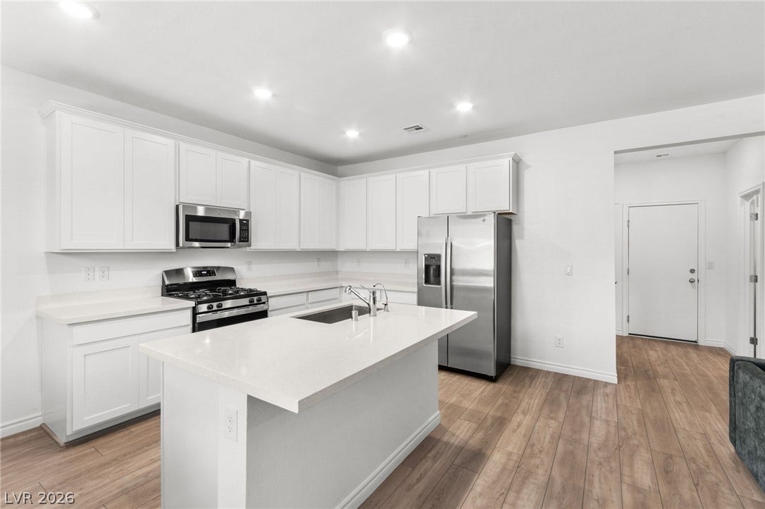 A well-lit kitchen features bright white cabinetry and stainless steel appliances.