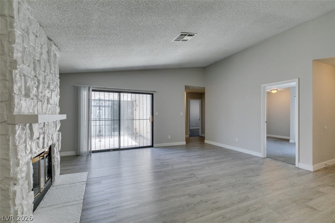 A spacious living area featuring a stone fireplace and light-colored flooring.