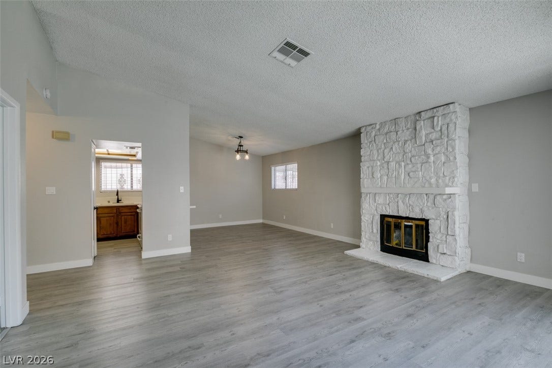 A spacious living room features light wood flooring and a grand stone fireplace.